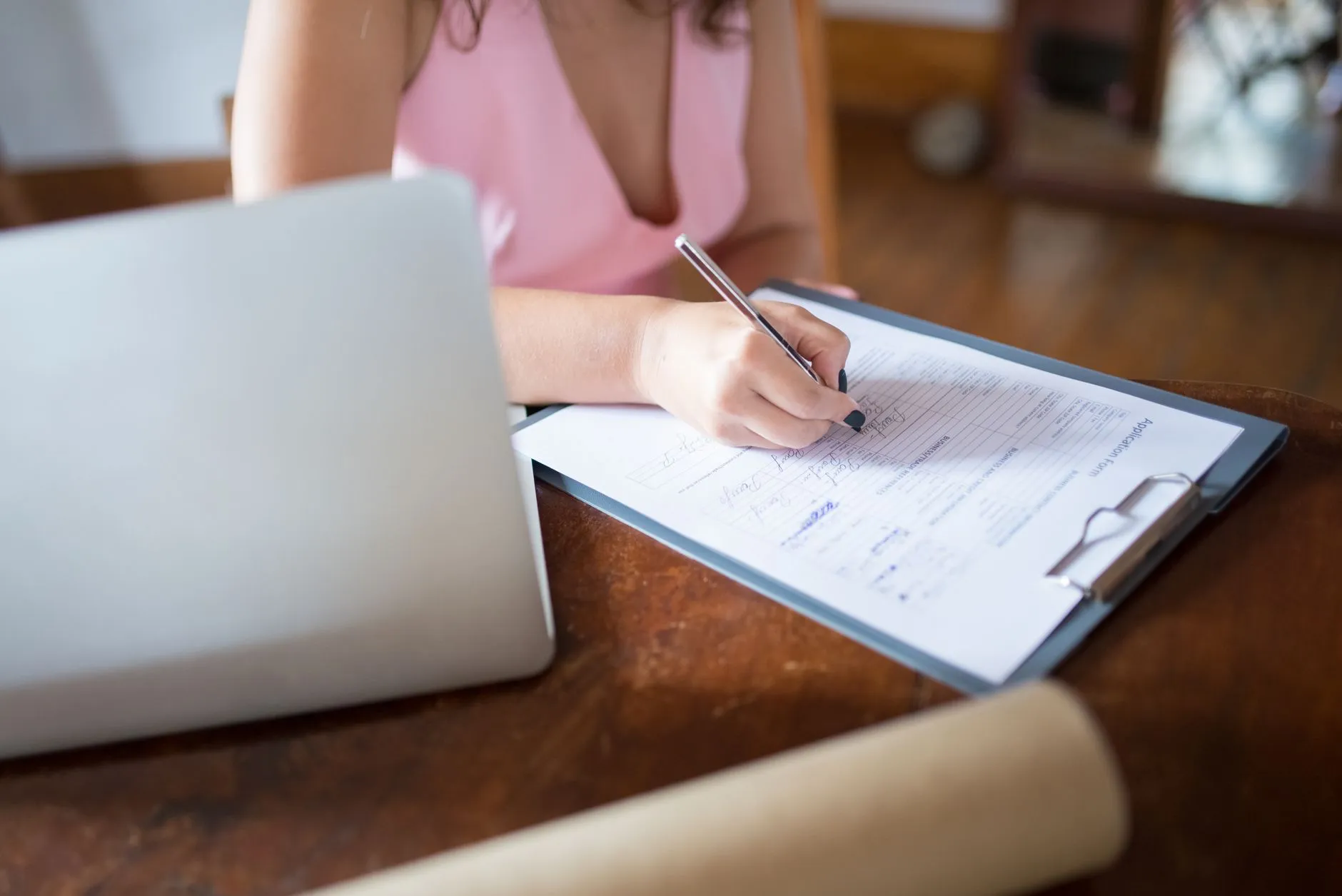 Persona llenando un formato de consentimiento informado junto a su laptop en el escritorio.