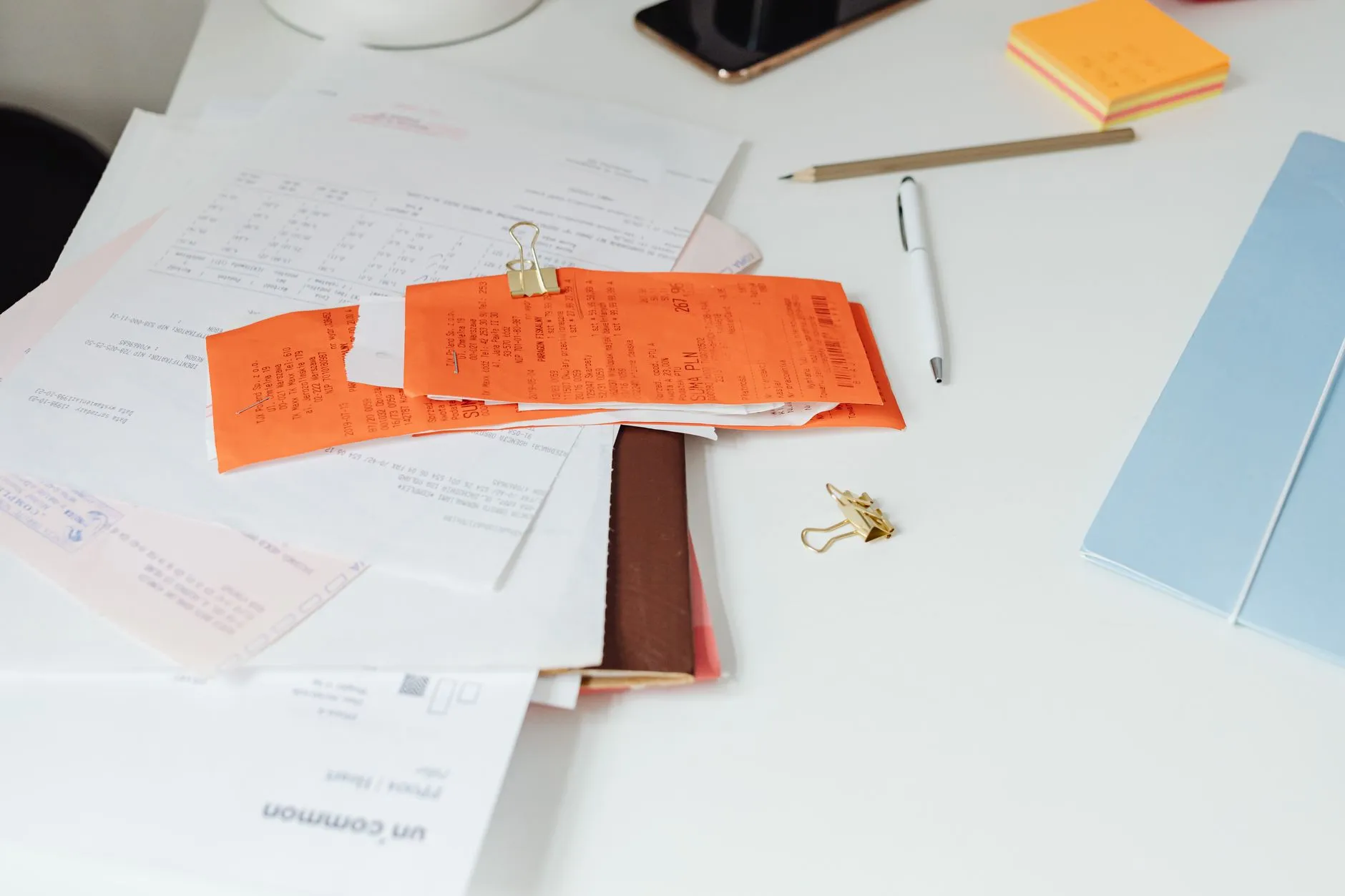 Recibos y papeles de cobro amontonados sobre un escritorio, junto a una libreta y un teléfono.