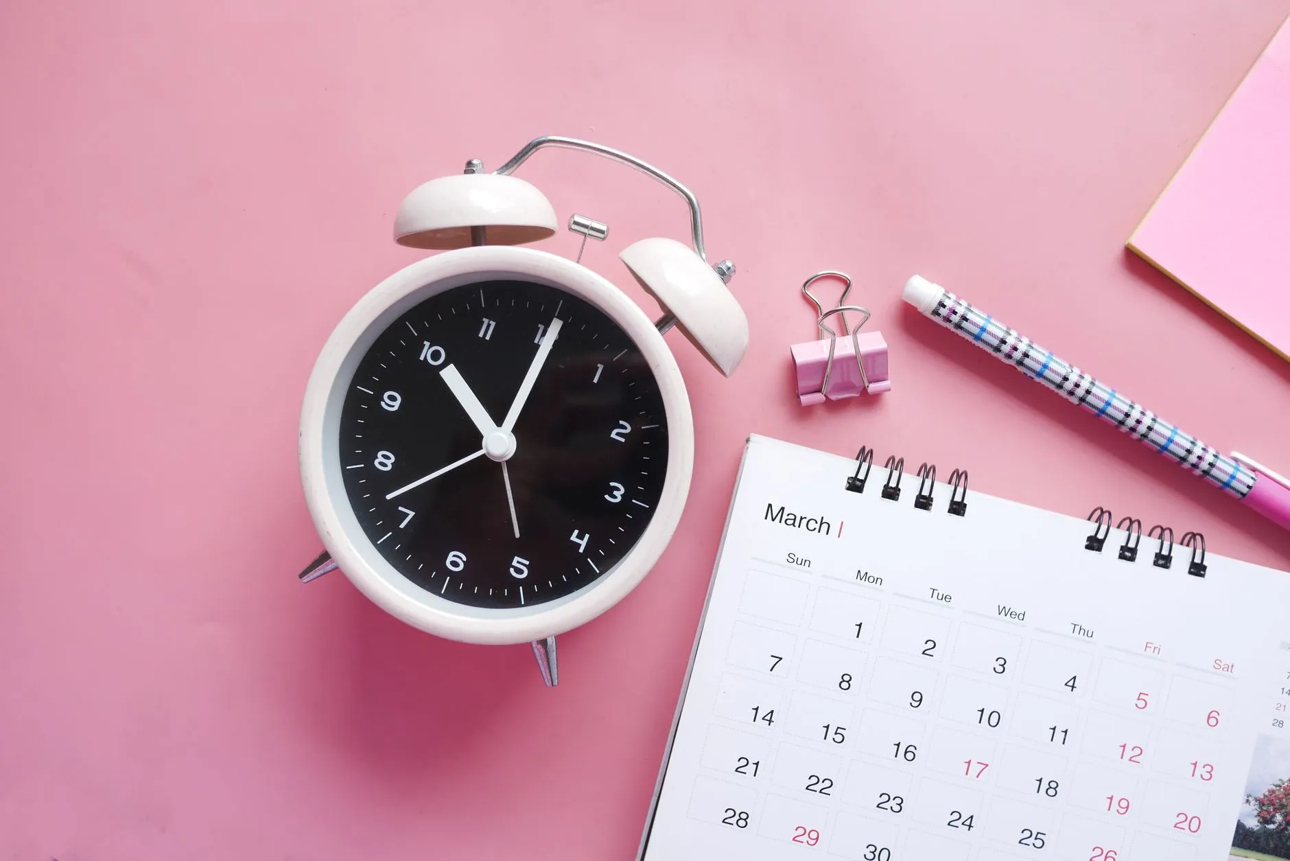 Reloj despertador junto a un calendario, representando el momento adecuado para enviar el recordatorio.